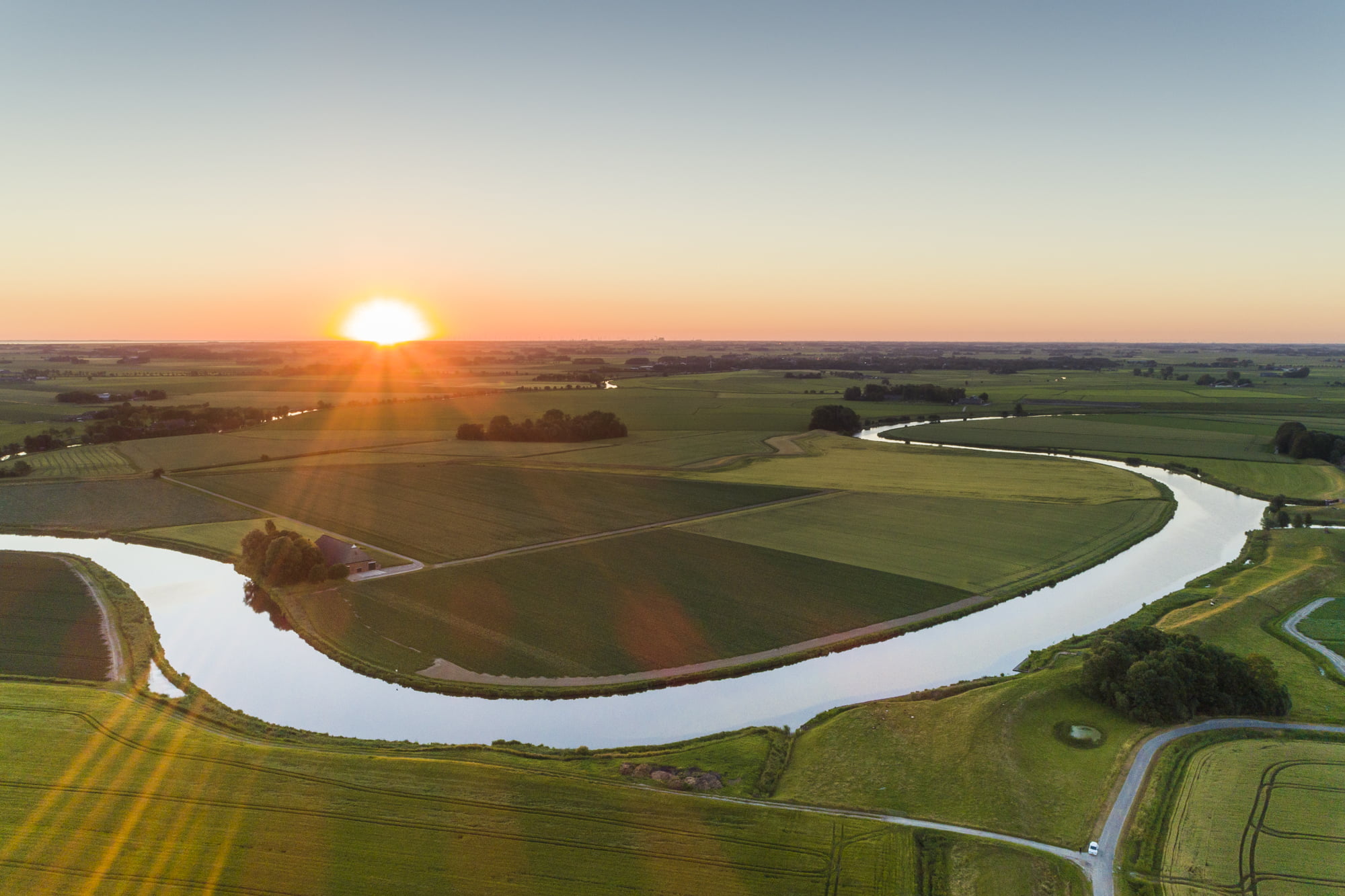 Een rivier slingert zich een weg door het vlakke land bij zonsopkomst