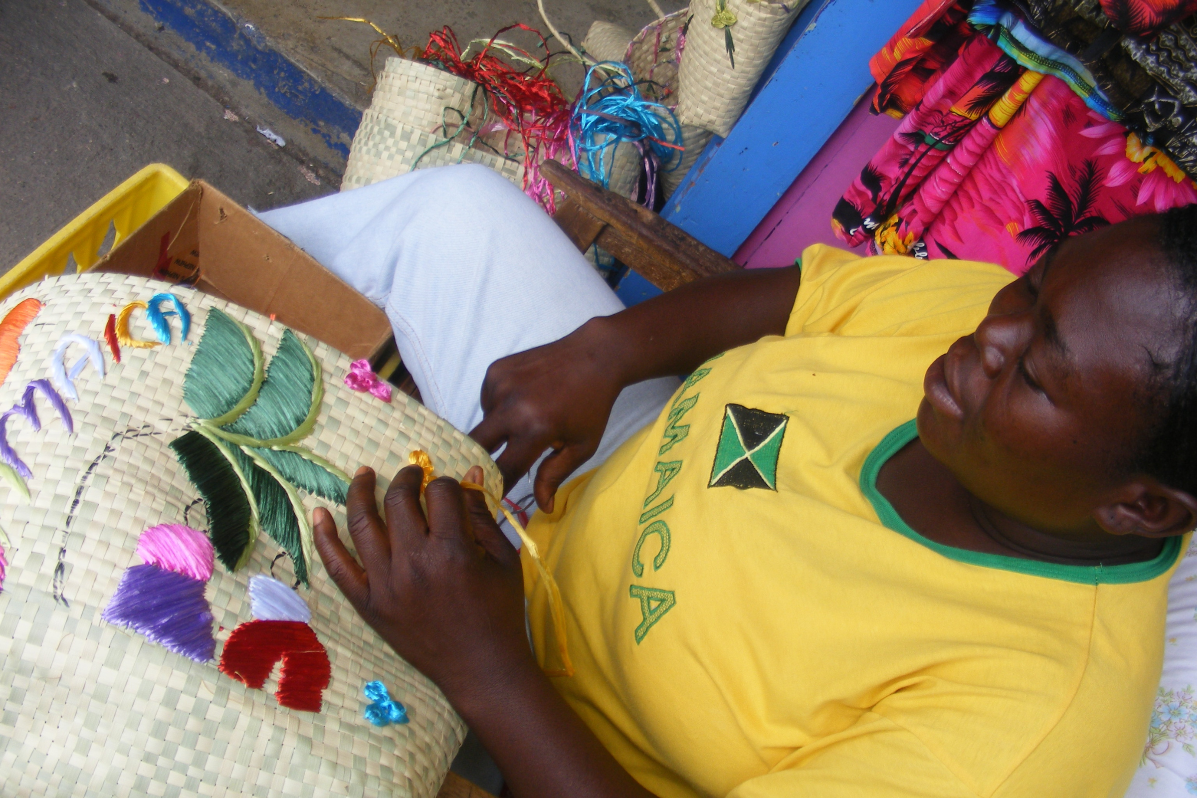 Een Jamaicaanse vrouw borduurt een ontwerp op een rieten tas.