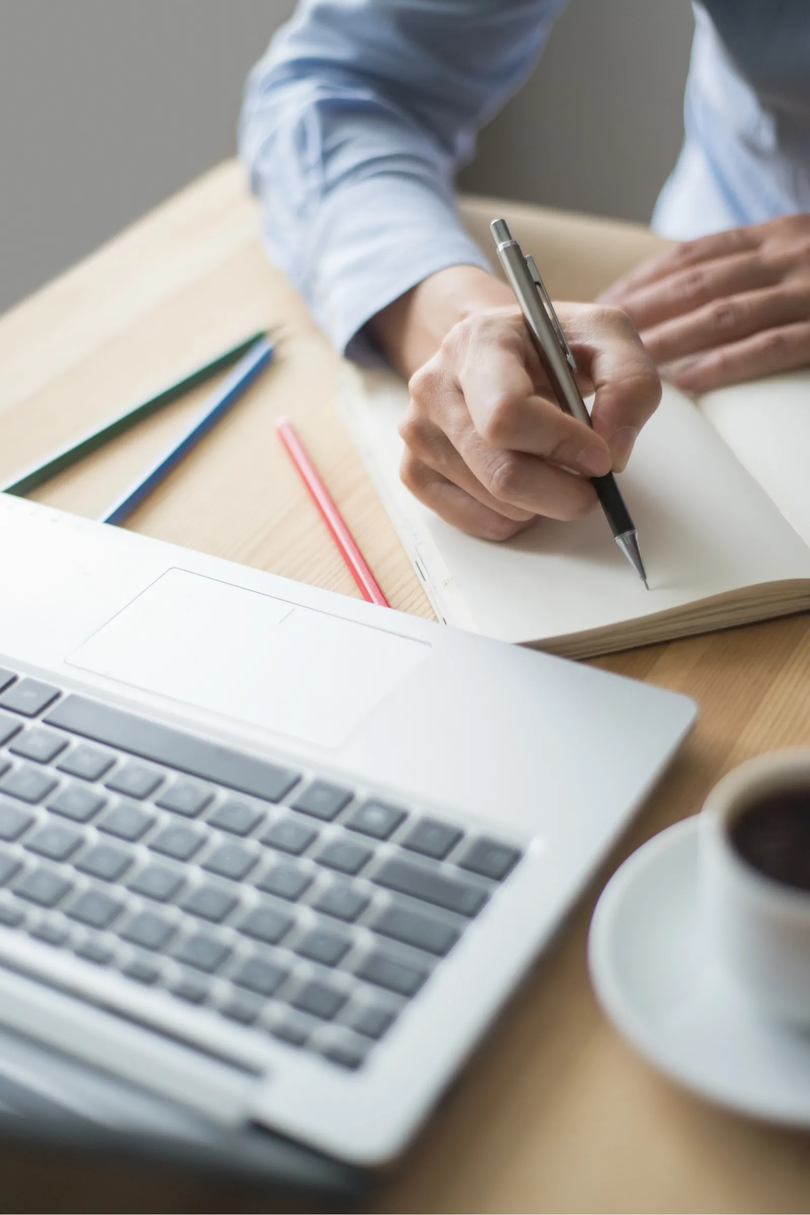 Afbeelding van laptop met ernaast iemand die schrijft in een notitieboek