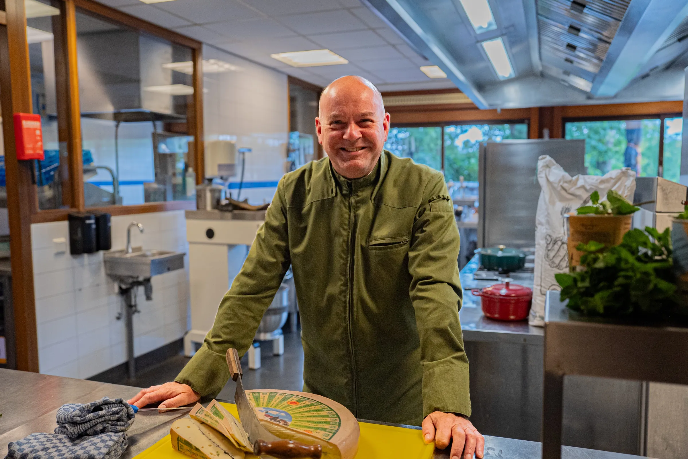 Kok staat in de keuken met een stuk kaas voor zich