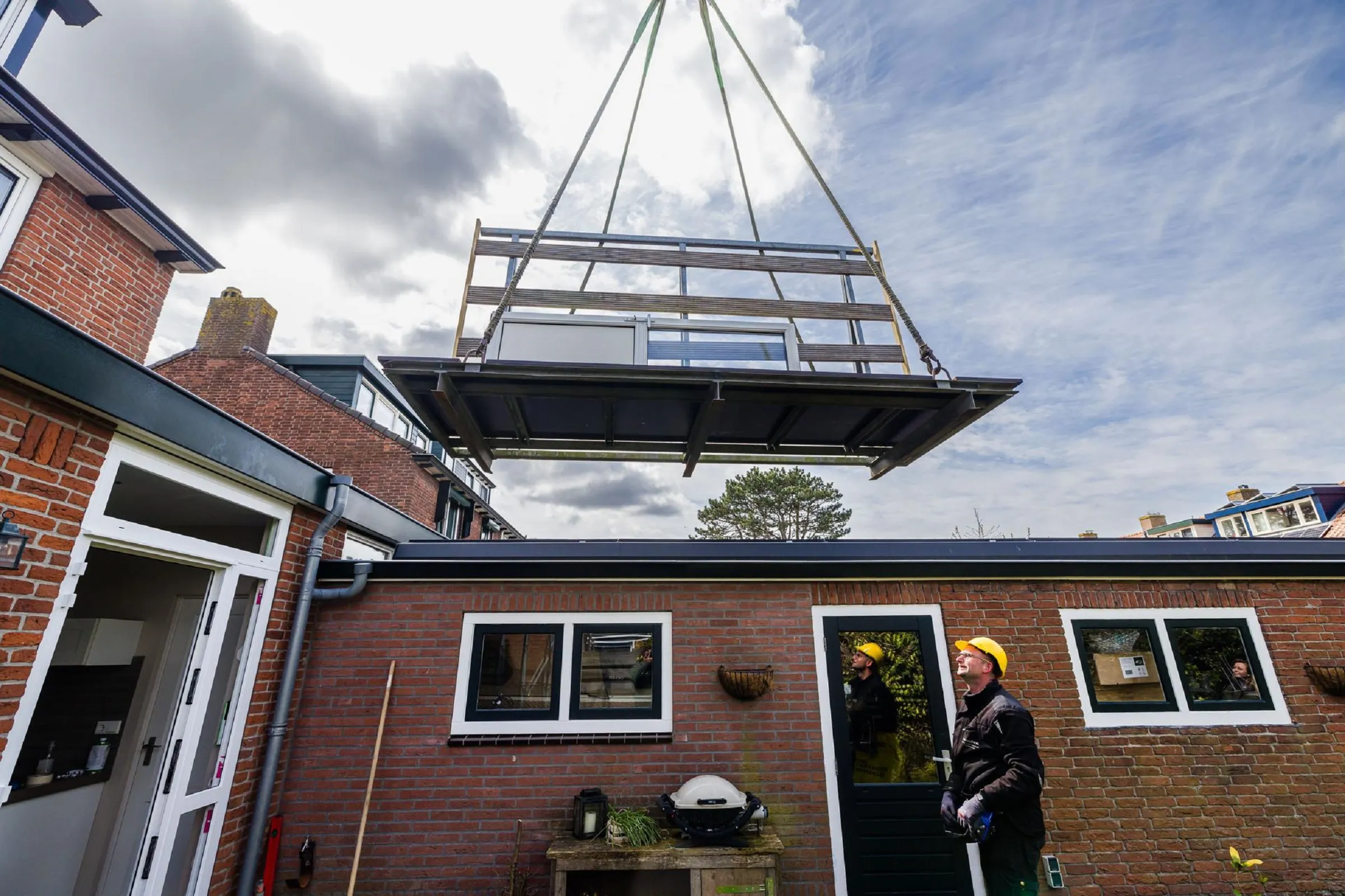 Een nieuwe glasplaat wordt door door een kraan richting een woning gedragen