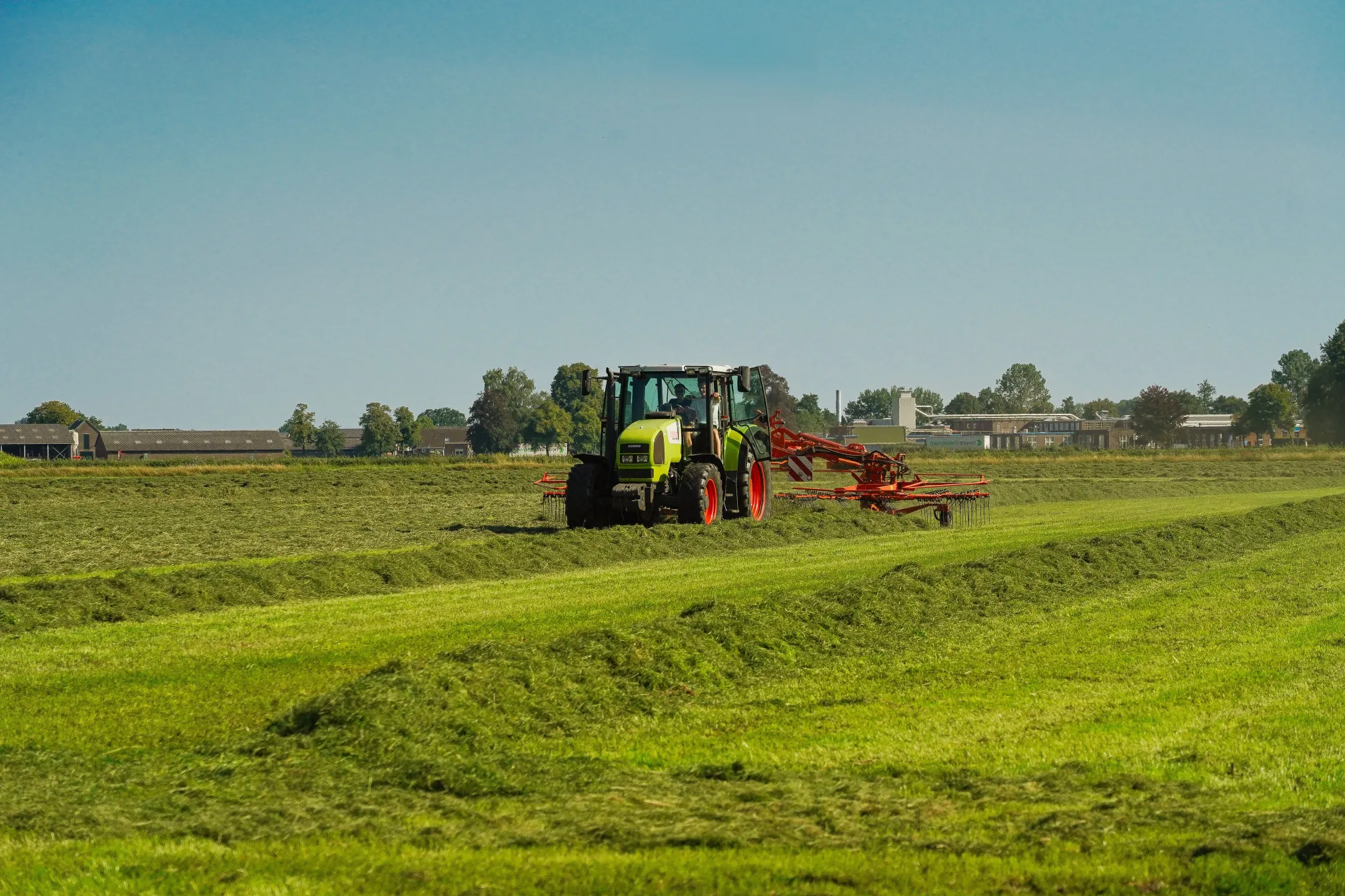 Weide in de zomer met een tractor met hooischudder